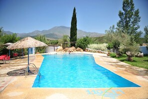 Una piscina con agua cristalina azul, rodeada por una terraza de piedra y con vistas a montañas al fondo.