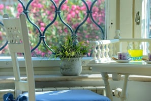 Una ventana con una reja metálica, una planta en maceta y una mesa con una taza y un platito.