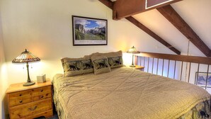 A bedroom with a large bed, two nightstands, a wooden dresser, a framed picture of Yosemite Valley, and a sloped ceiling with exposed beams. - (A211) Loft Condominiums (Yosemite National Park)