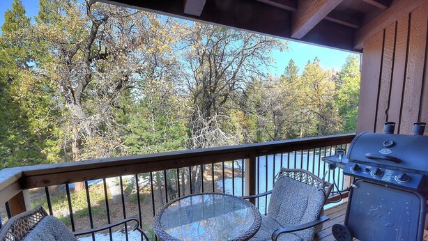A deck with a glass-top table and two patterned chairs, overlooking a wooded area. - (A211) Loft Condominiums (Yosemite National Park)