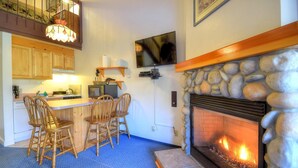 A cozy kitchen with wooden cabinets, a stone fireplace, and a dining area with wooden chairs. - (A211) Loft Condominiums (Yosemite National Park)