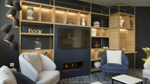 A modern living room with a fireplace, comfortable seating, and a large TV mounted on the wall. - Appart'hôtel Odalys City - Le Mans Centre Palais des Congrès (Le Mans)