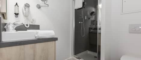 Un baño moderno con ducha envuelta en vidrio, un lavabo blanco con toalla y un espejo.
