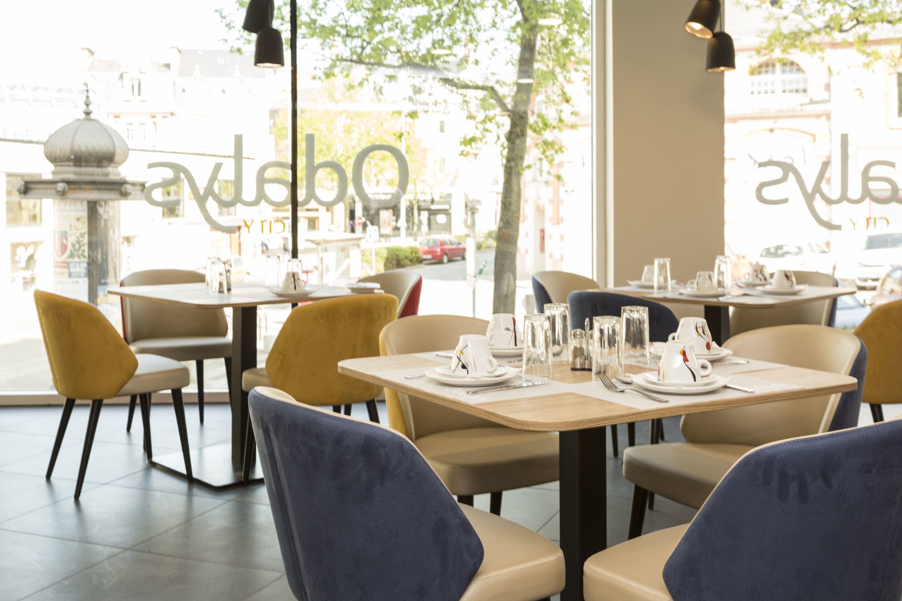 Interior de un restaurante con mesas dispuestas para comer, sillas y vistas a la calle.