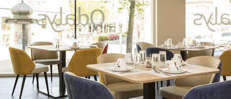 Interior de un restaurante con mesas dispuestas para comer, sillas y vistas a la calle.