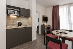 Una cocina moderna con microondas, hervidor de agua y pileta. Hay una zona de comedor con mesa y sillas, y un televisor montado en la pared.