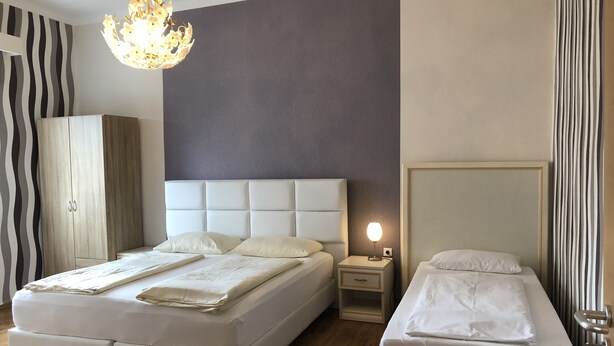 Ein Hotelzimmer mit einem großen Bett, einem kleineren Bett, einem Kleiderschrank, einem Nachttisch und einer Kristallleuchter.