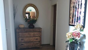 Ein Flur mit Holzboden, einem roten Teppich, einer Holzkommode mit Spiegel, einer Topfpflanze und einem gerahmten Kunstwerk an der Wand.