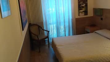 Un dormitorio con cama, una silla, un cuadro y un televisor en la pared.