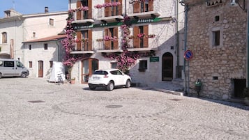 Una strada acciottolata con un'auto bianca parcheggiata di fronte a un edificio con balconi decorati da fiori rosa.