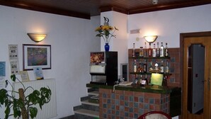 A bar area with a counter, a coffee machine, and a shelf with bottles. There is a chair and a table in the foreground. - Hotel Ai 4 Camosci (Civitella Alfedena)
