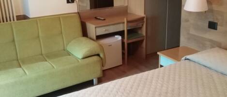 Un dormitorio con cama, sofá verde, escritorio con espejo y armario.