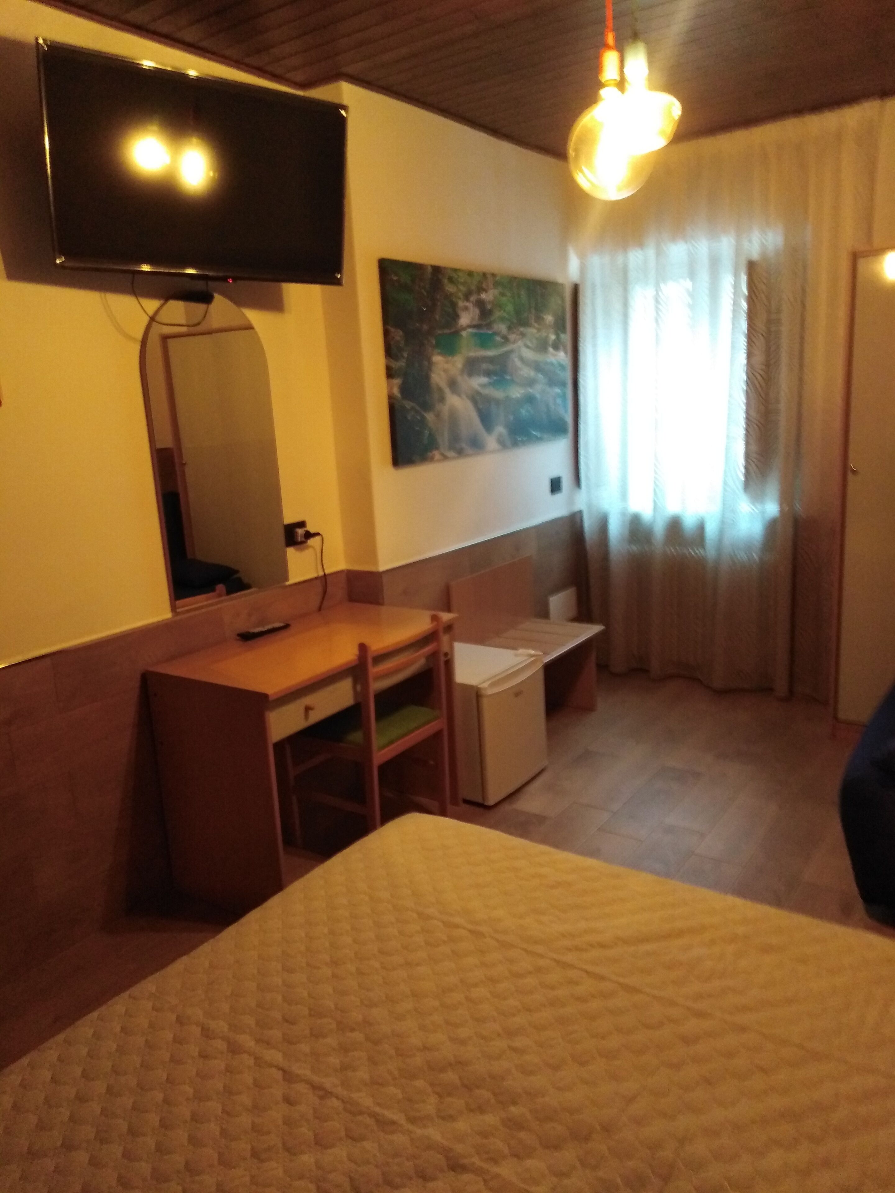 A hotel room with a bed, a desk, a chair, a television mounted on the wall, and a painting.