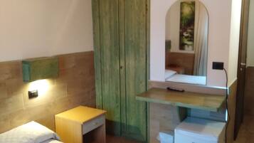 Un dormitorio con cama, mesita de noche de madera, escritorio con espejo y armario verde.