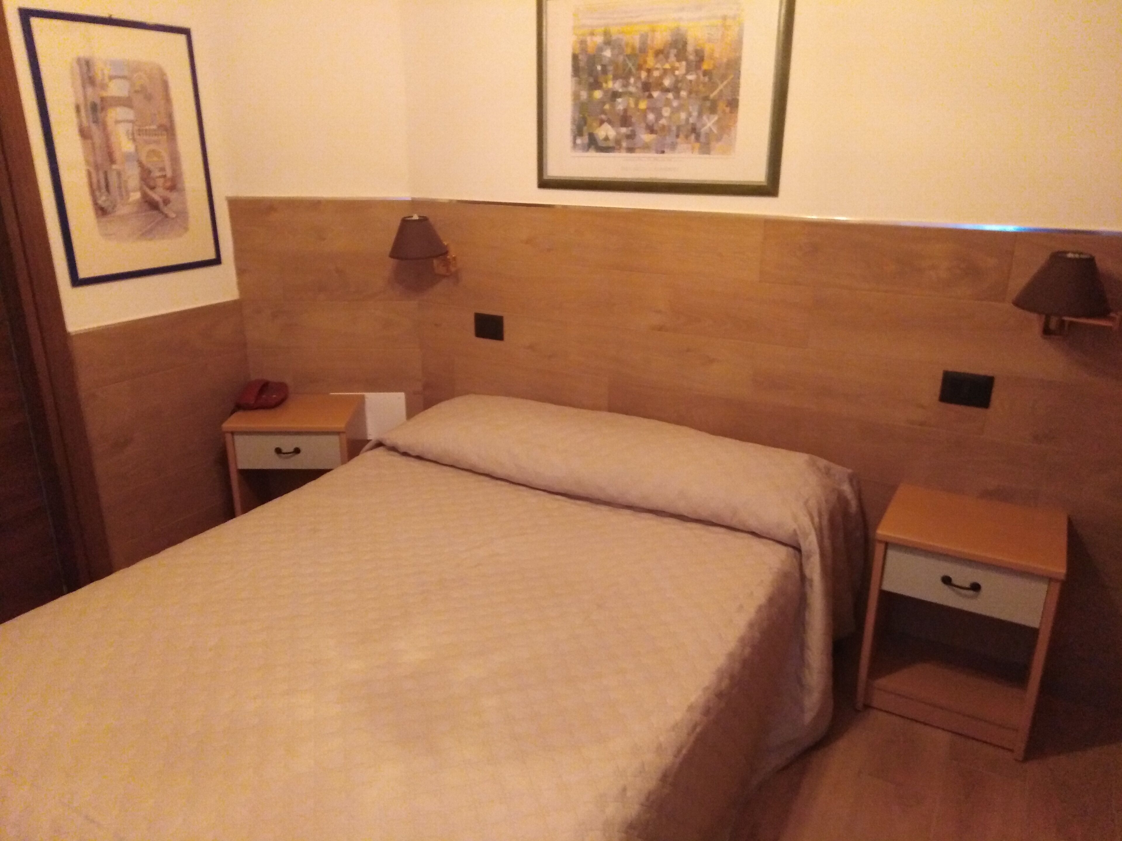 Una cama bien hecha con una colcha color beige en una habitación de hotel. Hay dos mesitas de noche, cada una con una lámpara y un cajón.