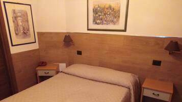 Ein ordentlich bezogenes Bett mit einer beige-farbenen Tagesdecke in einem Hotelzimmer. Es gibt zwei Nachttische, jeder mit einer Lampe und einer Schublade.