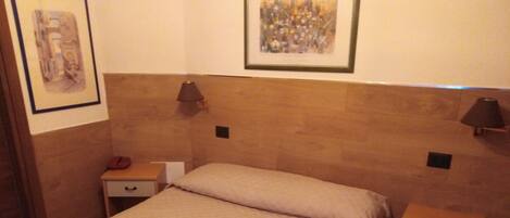 Una cama bien hecha con una colcha color beige en una habitación de hotel. Hay dos mesitas de noche, cada una con una lámpara y un cajón.