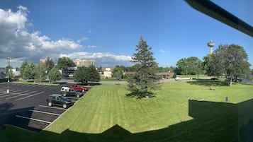 A parking lot with several cars, a grassy area, and buildings in the background.