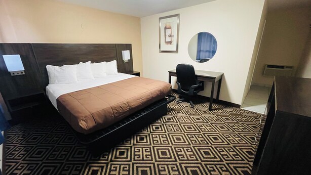 A hotel room with a bed, a desk, a chair, and a patterned carpet.