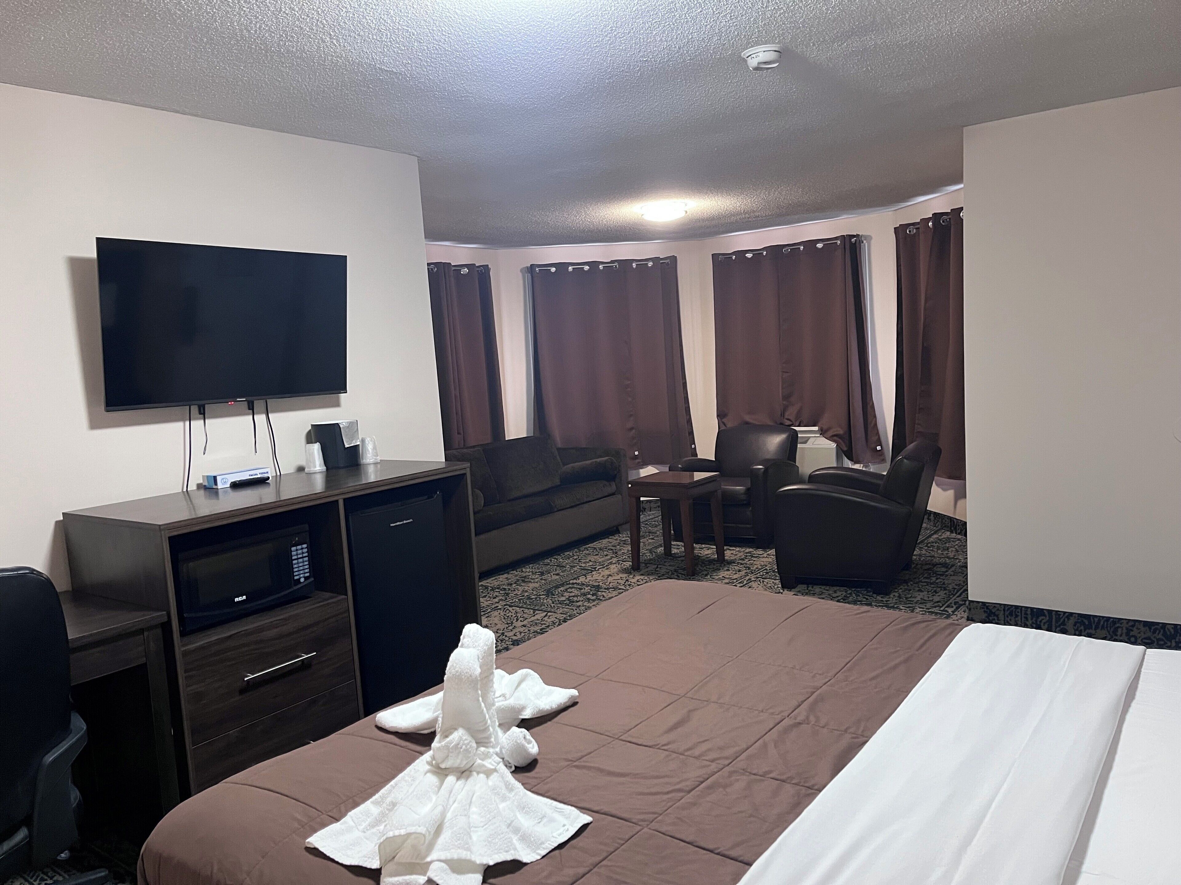 A hotel room with a bed, a desk with a flat-screen TV, a chair, a sofa, and a small table.