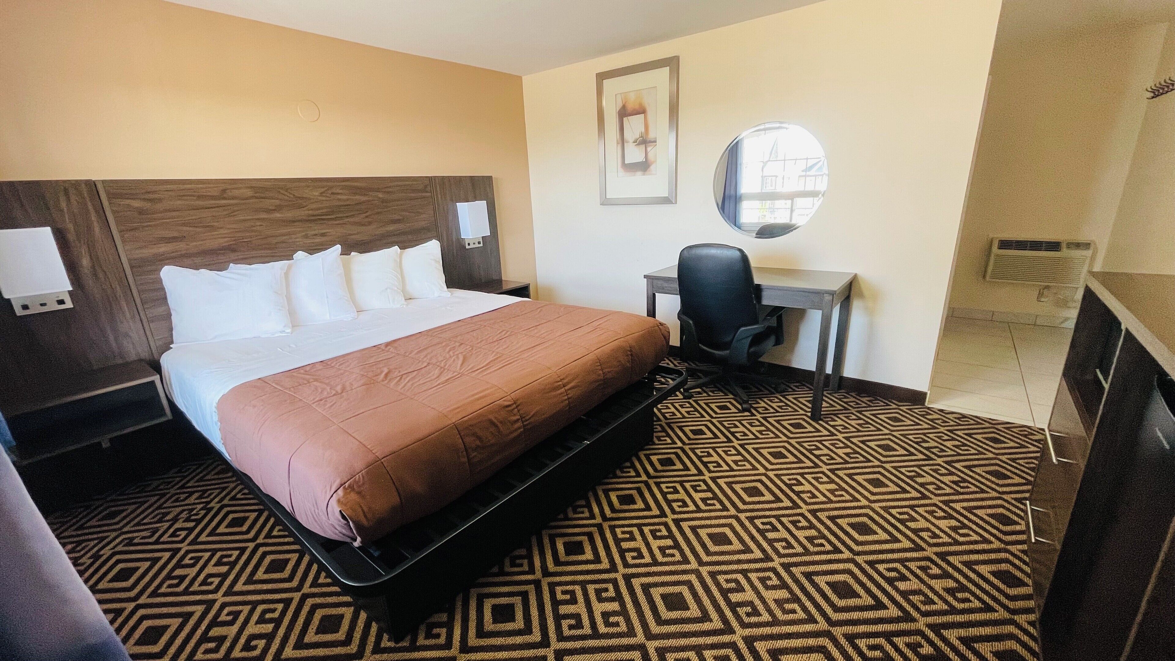 Une chambre d’hôtel avec un grand lit, un bureau, une chaise, un miroir et une moquette à motifs.
