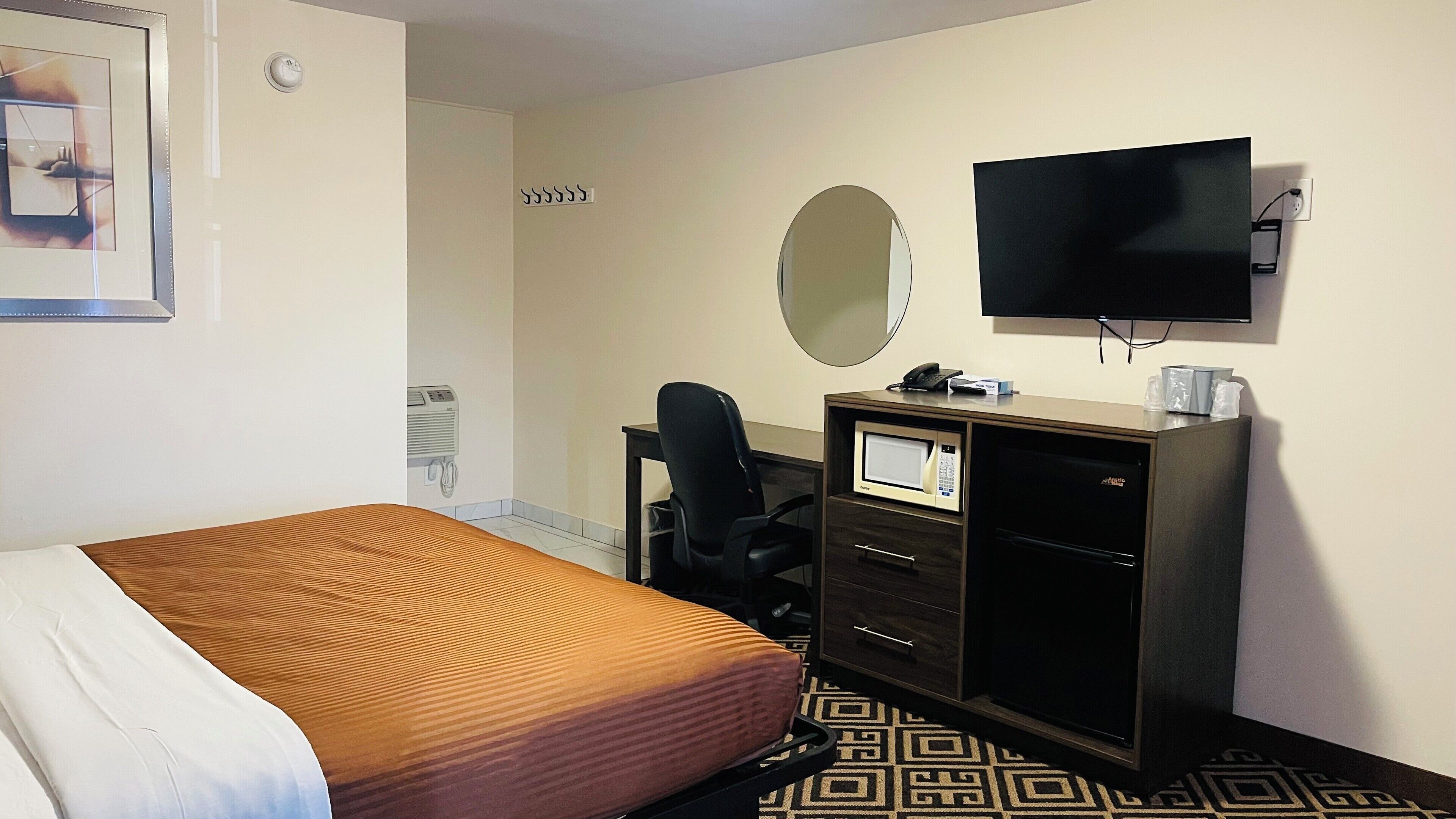 Una habitación de hotel con cama, escritorio, computadora, teléfono, televisión y espejo.