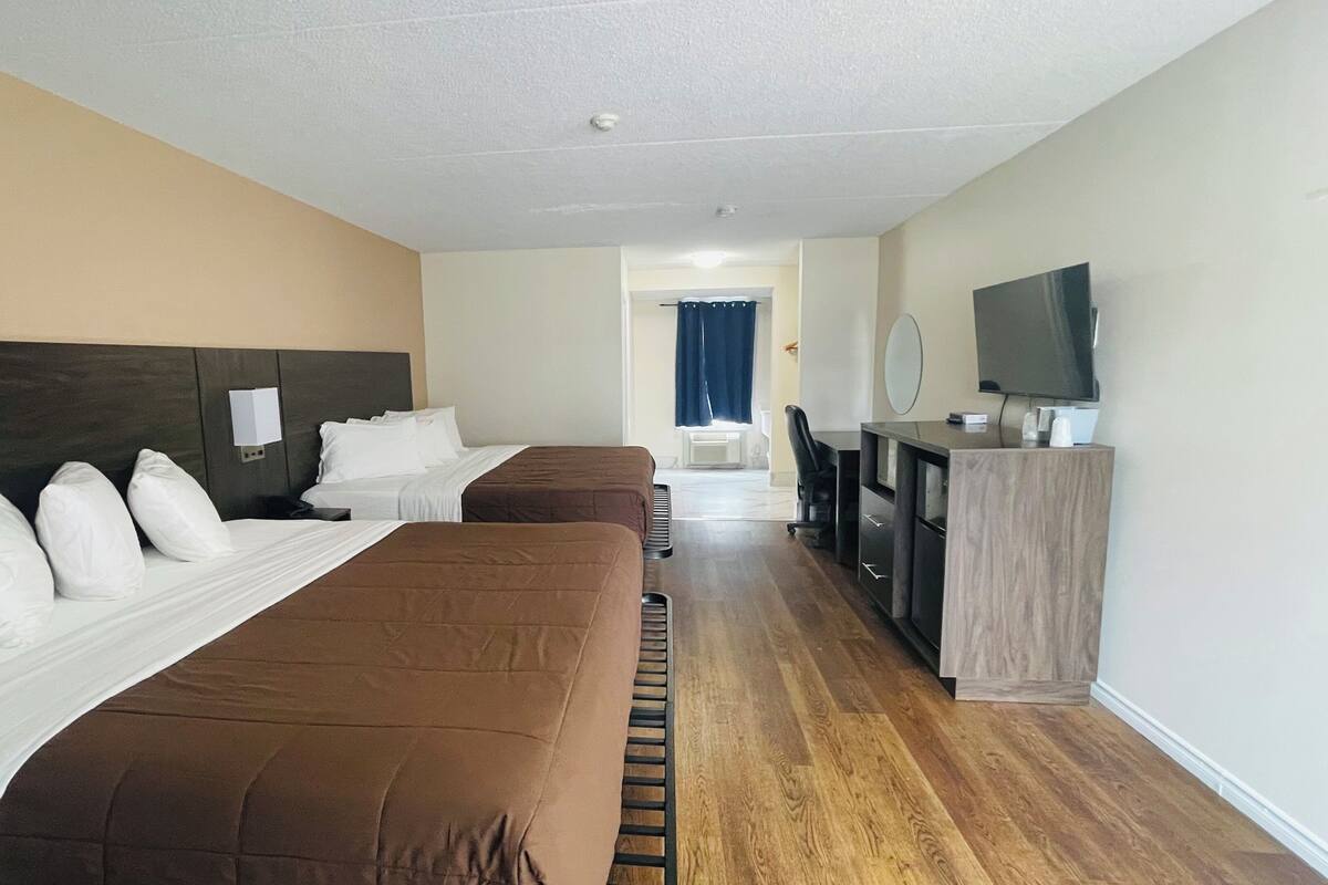 Une chambre d’hôtel avec deux lits, un bureau avec une télévision et une salle de bain à l’arrière-plan.