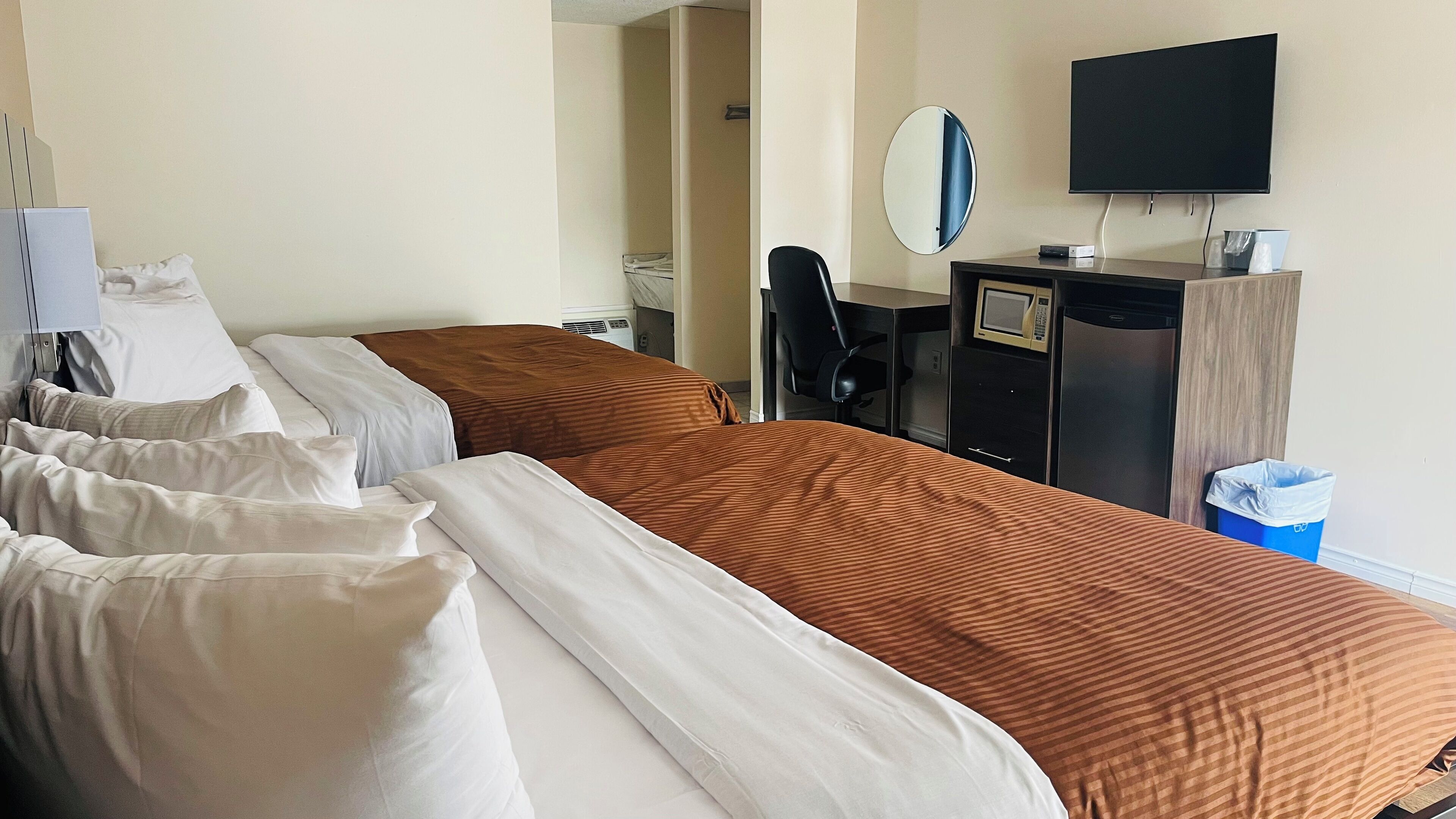 Habitación de hotel con dos camas, un escritorio con computadora, un televisor y un cesto de basura.