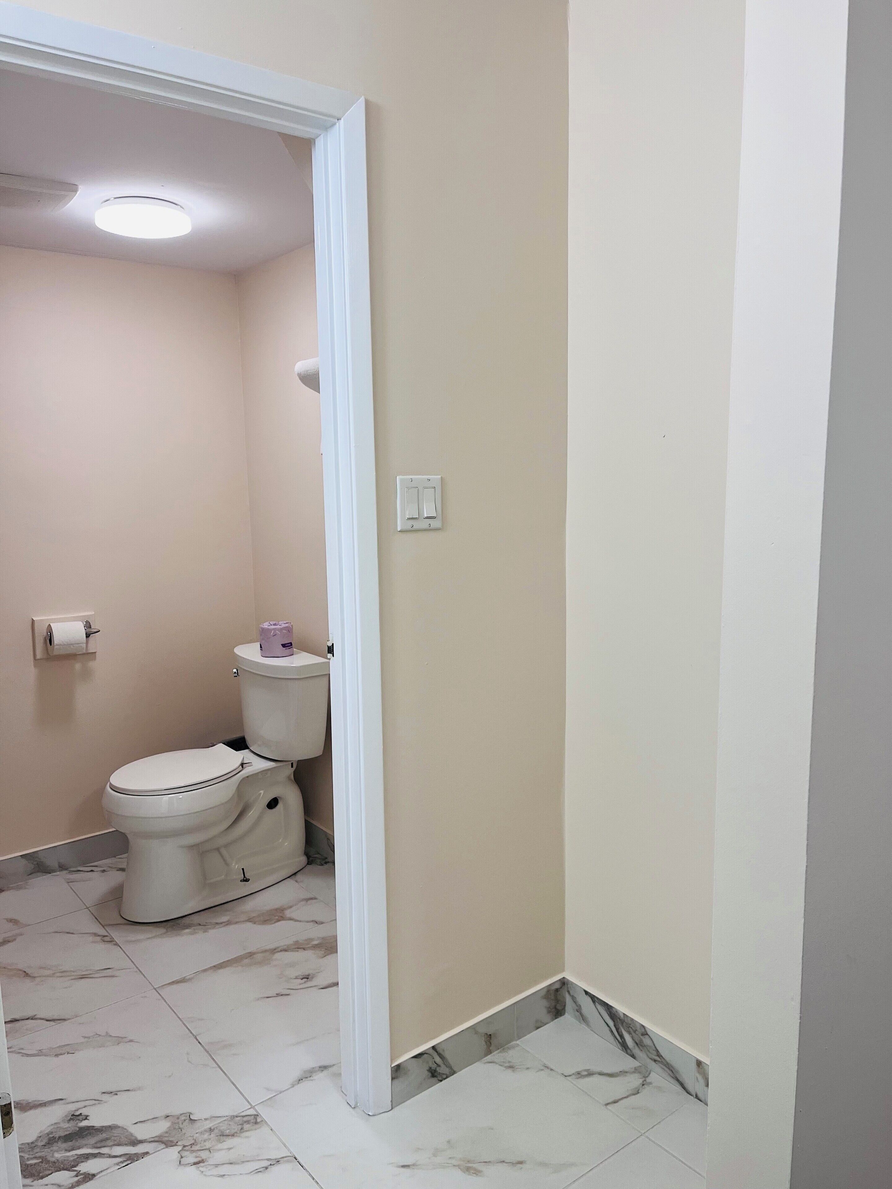 Un baño pequeño con inodoro, un rollo de papel higiénico y piso de baldosas de mármol.