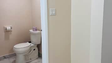 Un baño pequeño con inodoro, un rollo de papel higiénico y piso de baldosas de mármol.