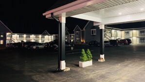 A parking area with multiple cars, a covered section, and a building with multiple windows and a staircase.
