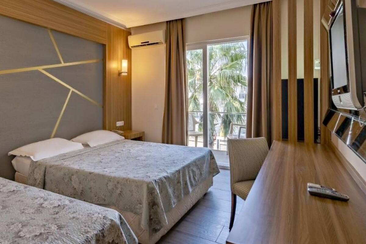 A hotel room with two beds, a desk, a chair, and a large window with a view of palm trees.