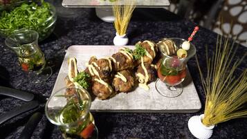 A dining table with a variety of food items, including skewered meat, a glass of drink with a garnish, and a bowl of greens.