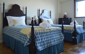 Una cama doble con cabecera de madera oscura, una mesita de noche con lámpara y una ventana con persianas.