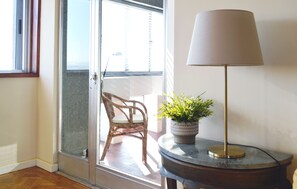 A room with a wicker chair near a sliding glass door, a potted plant on a round table, and a floor lamp.