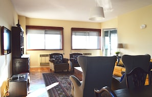 Una sala de estar con dos sofás, una mesa de centro, televisor y un ventanal con persianas.