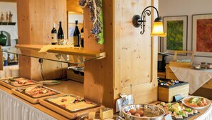A buffet setup with various food items, a wine selection, and a decorative wall piece. - Panoramahotel Grobauer (Spiegelau)