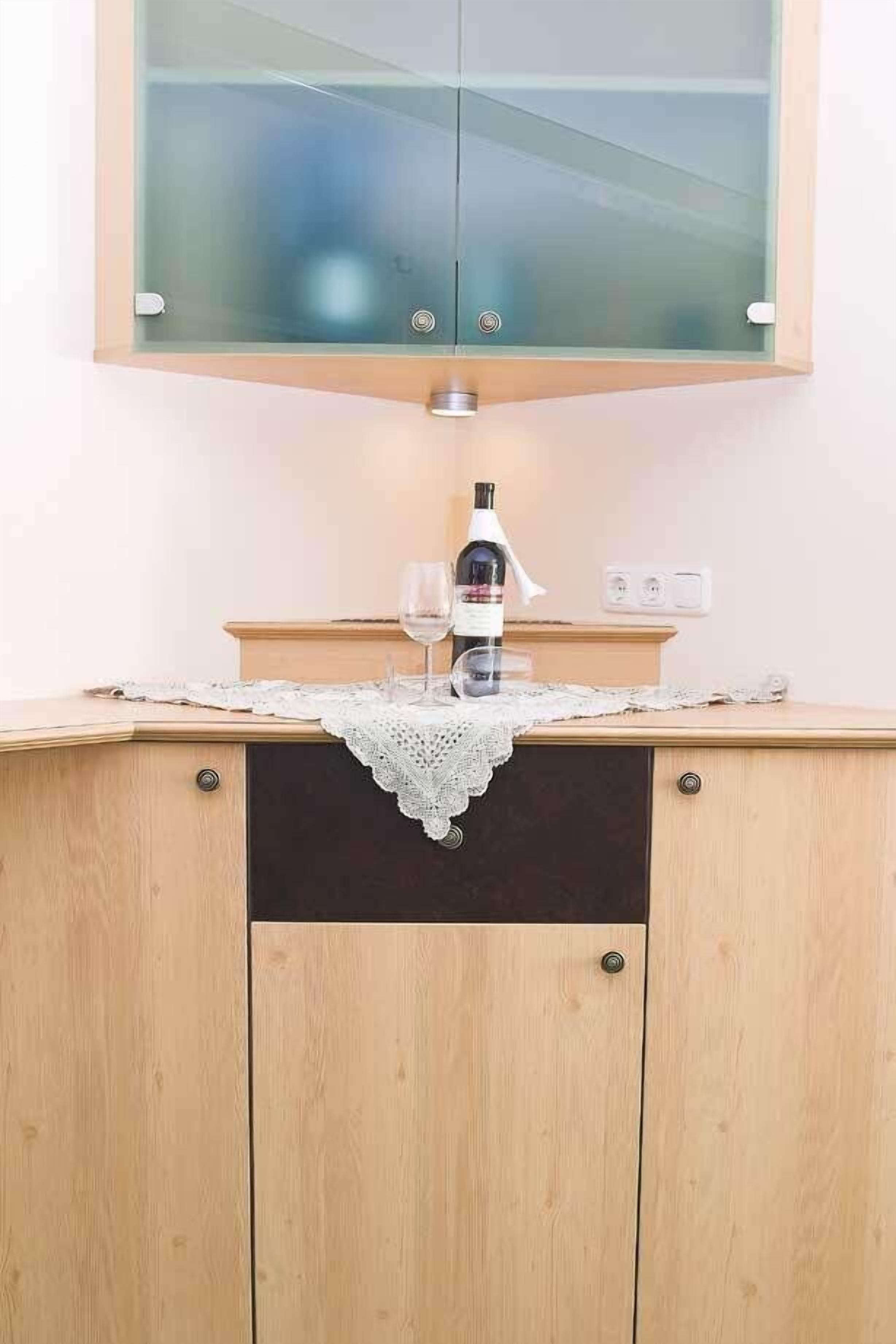 A kitchen with a wooden cabinet, a glass-fronted upper cabinet, and a wine bottle on the counter.