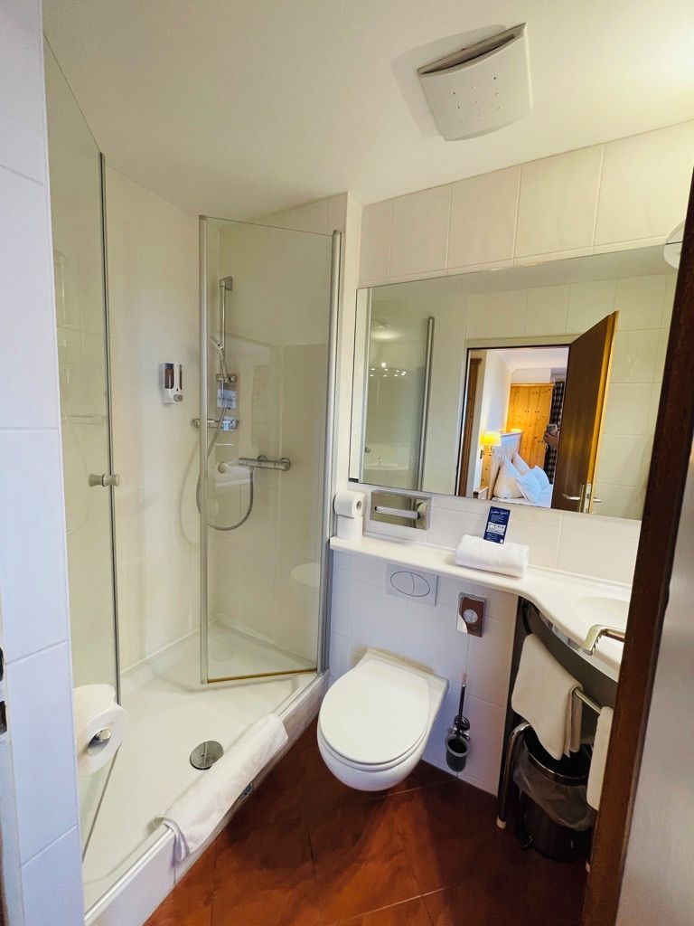 A modern bathroom with a glass shower enclosure, a toilet, and a sink with a mirror above.