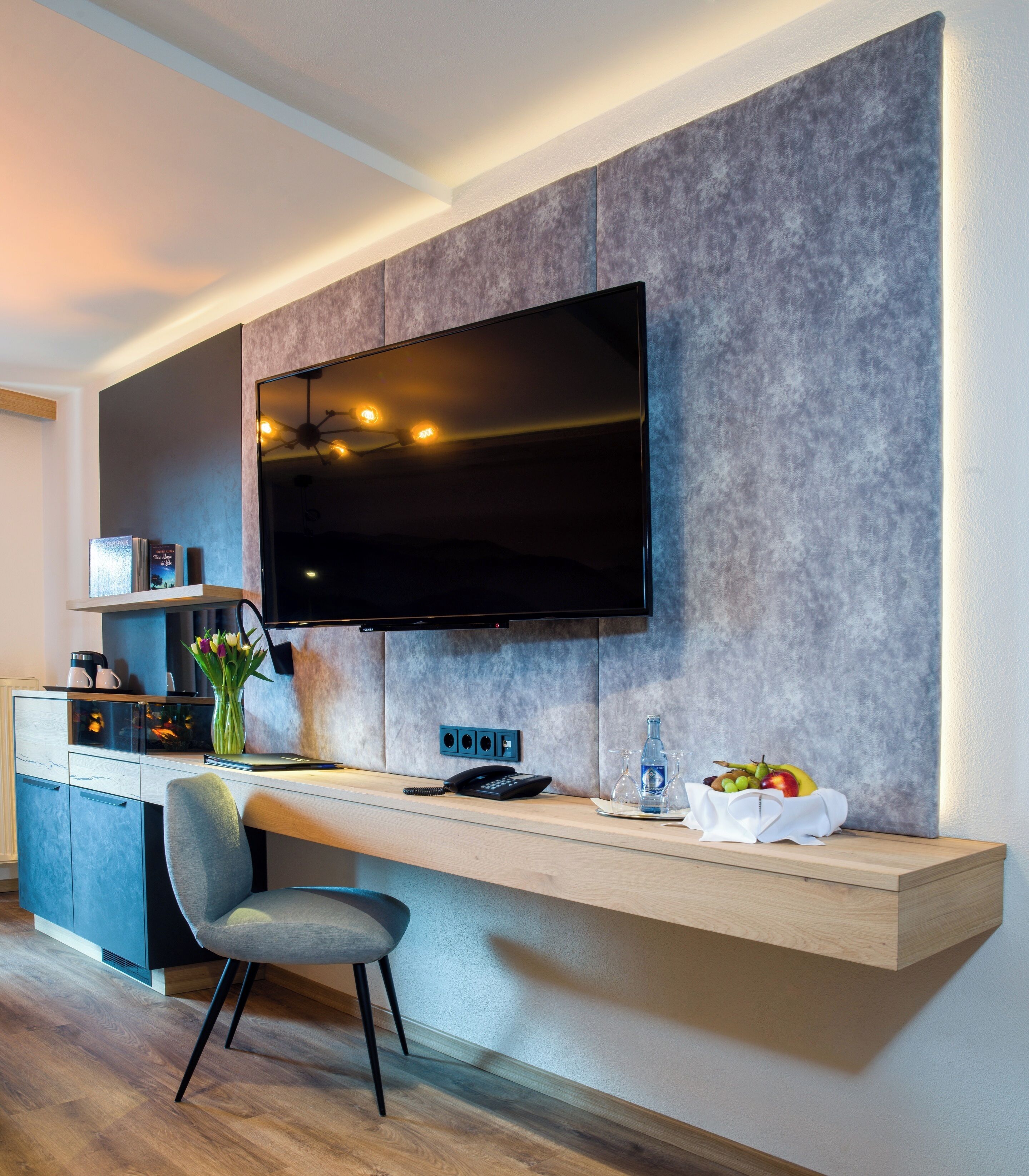 A modern kitchen with a built-in TV, wooden countertop, and a chair.