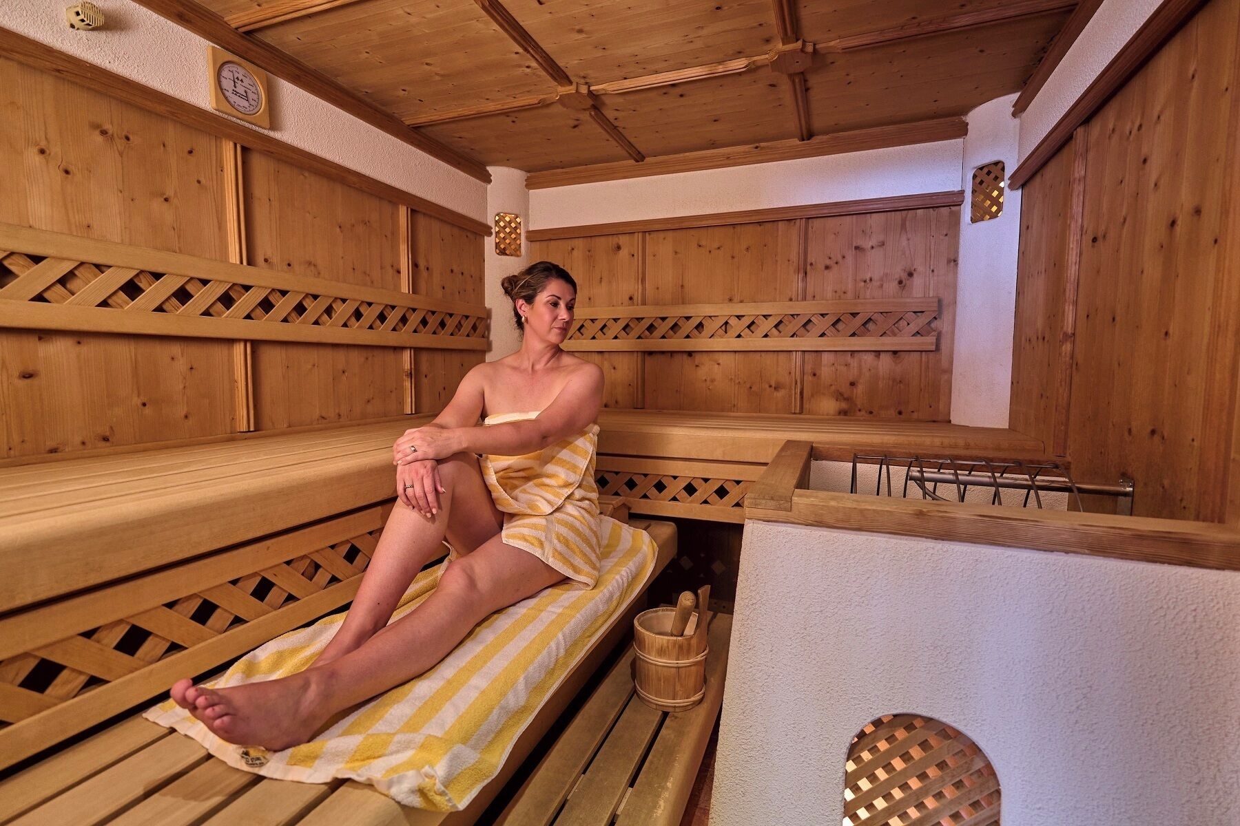 A wooden sauna with benches and a wooden bucket.