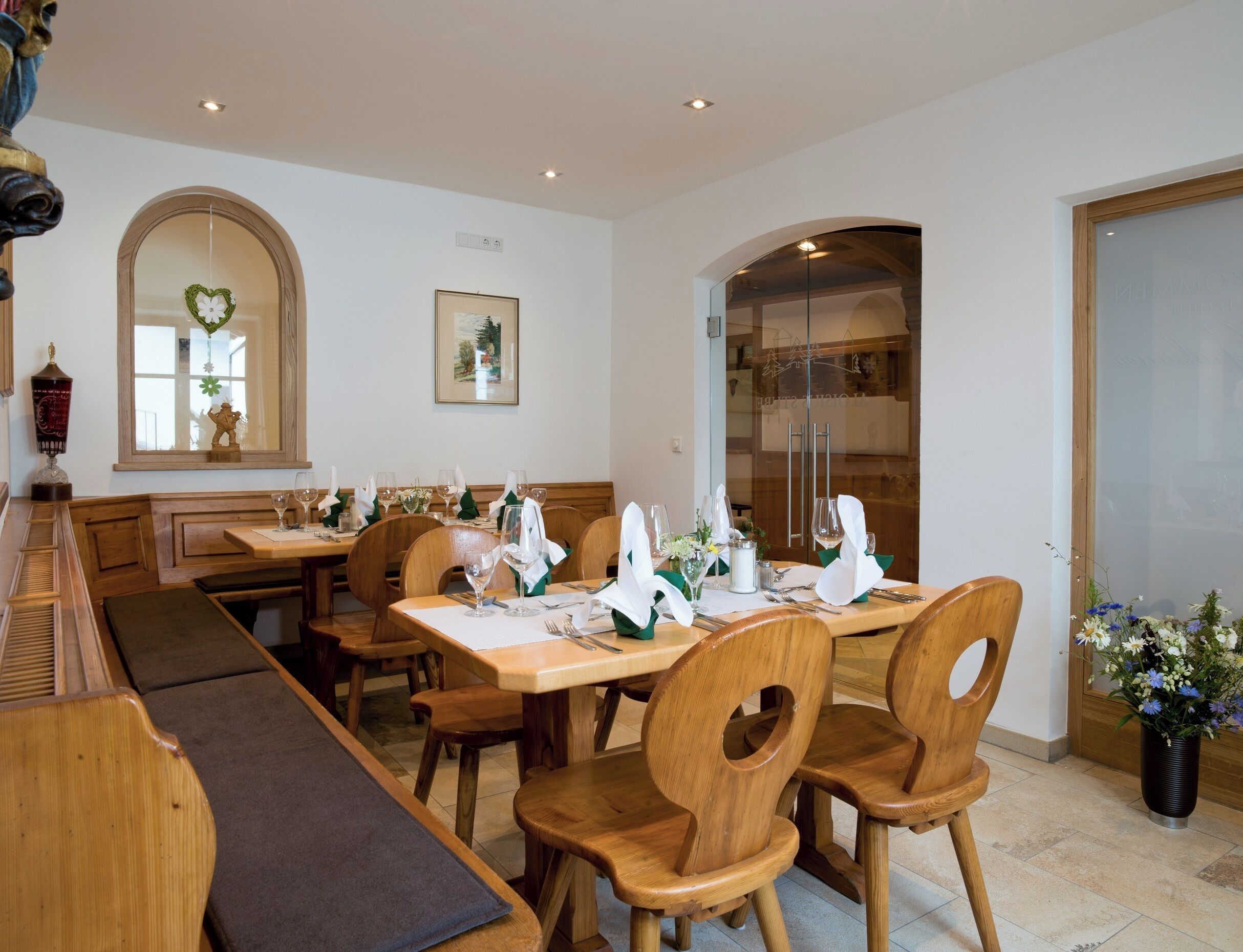 A restaurant with wooden tables and chairs, a long bench, and a decorative mirror.