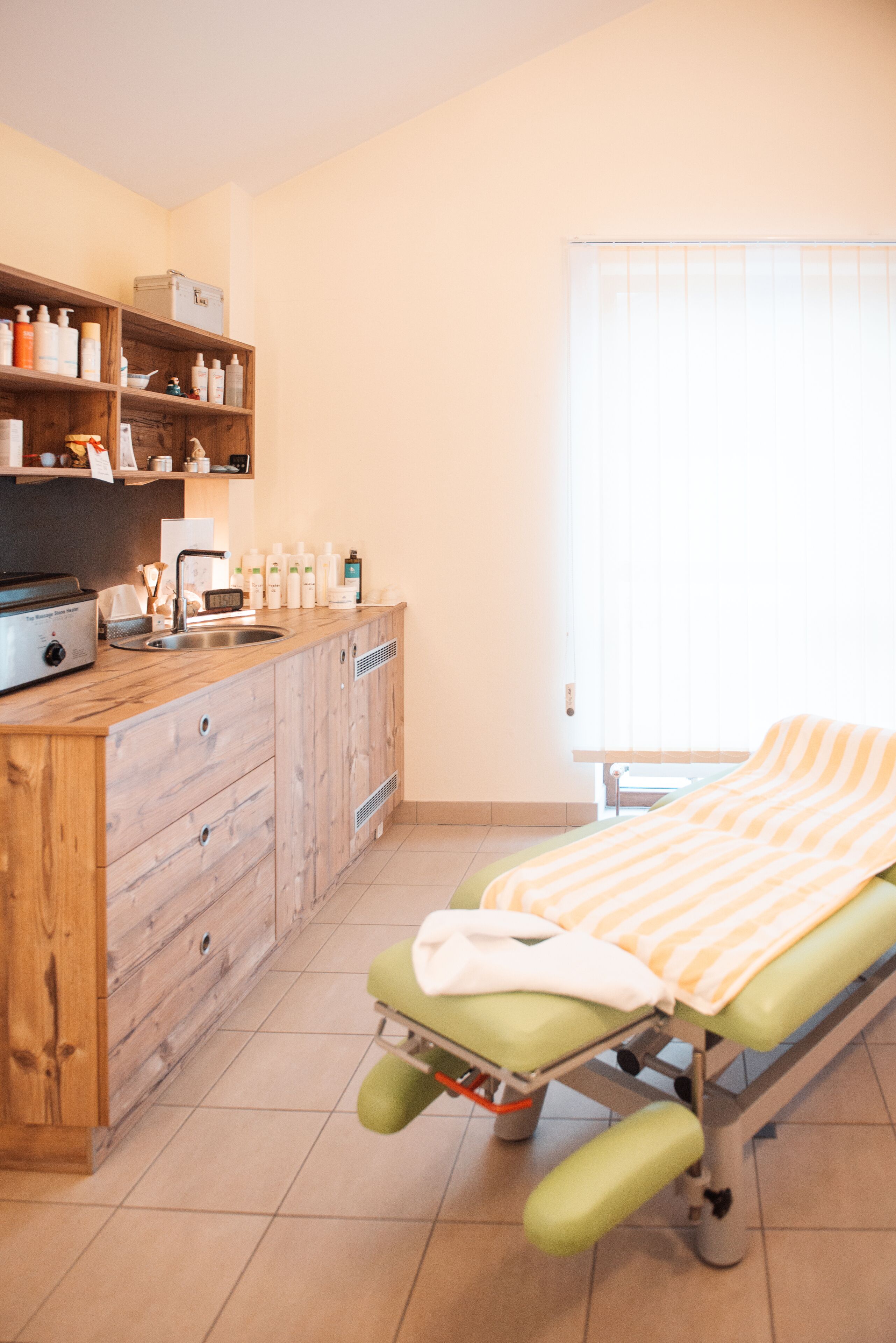 Une salle d’examen médical avec un meuble en bois, un lavabo et un lit recouvert d’une couverture à rayures.