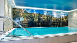 A swimming pool with a view of a forest and lake, surrounded by a modern interior with a skylight and circular windows. - Panoramahotel Grobauer (Spiegelau)