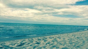 Uma praia com areal arenoso e mar calmo sob céu nublado.
