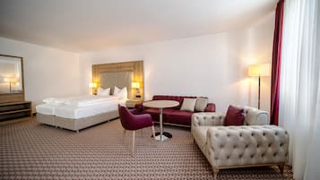 Ein Hotelzimmer mit einem Bett, einem roten Sofa, einem beigefarbenen Sessel, einem kleinen runden Tisch und einer Lampe.