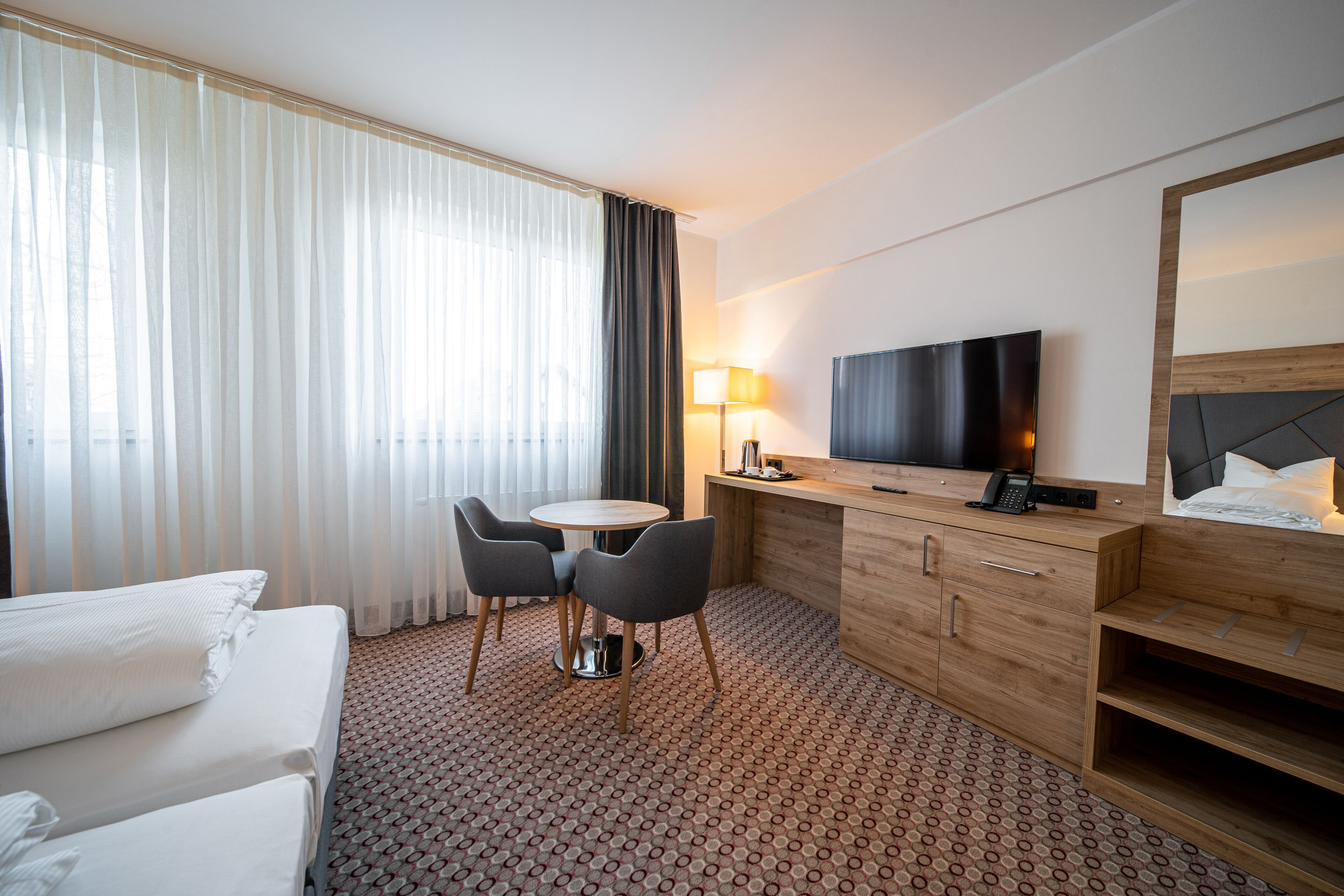 A hotel room with a bed, a desk with a TV, a lamp, and a chair.