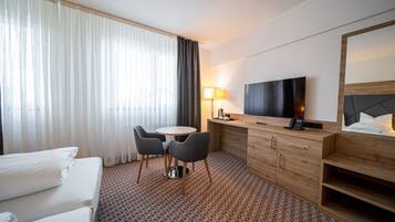 A hotel room with a bed, a desk with a TV, a lamp, and a chair.