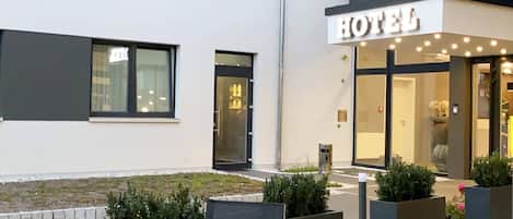 A modern hotel exterior with a prominent 'HOTEL' sign, outdoor seating, and a well-maintained garden area.