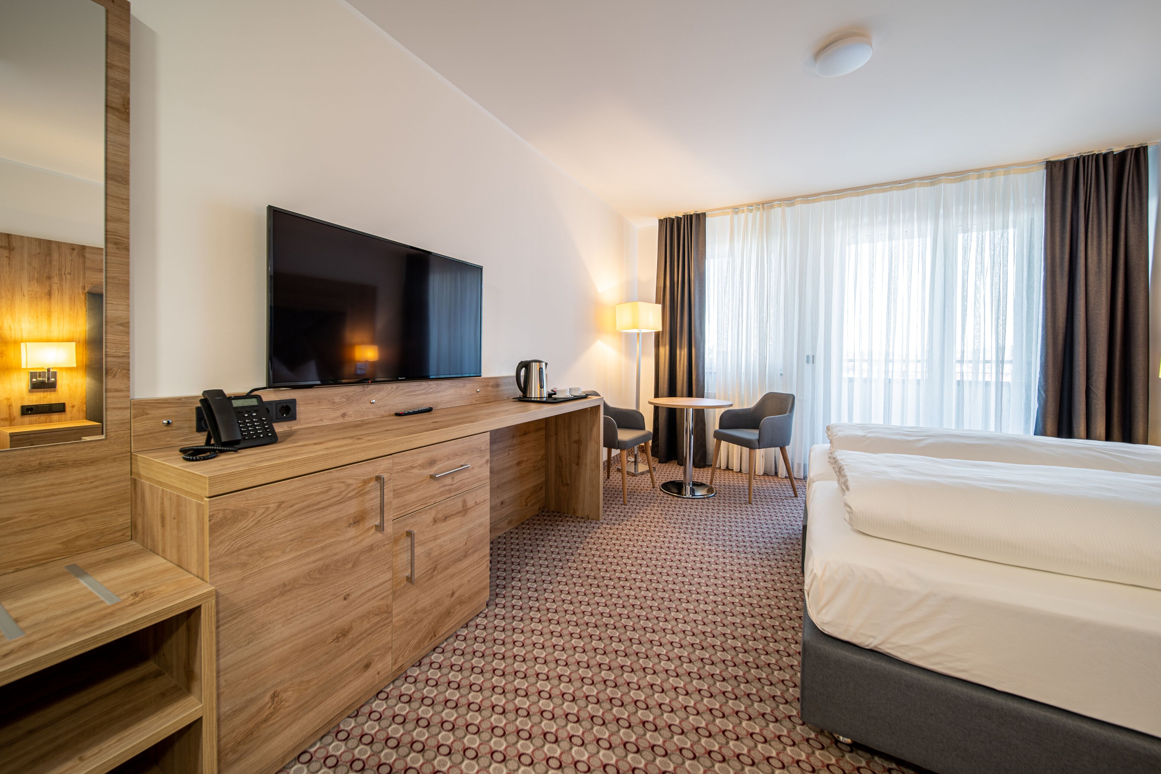 Habitación de hotel con una cama, un escritorio con televisor de pantalla plana, teléfono, lámpara y una silla.